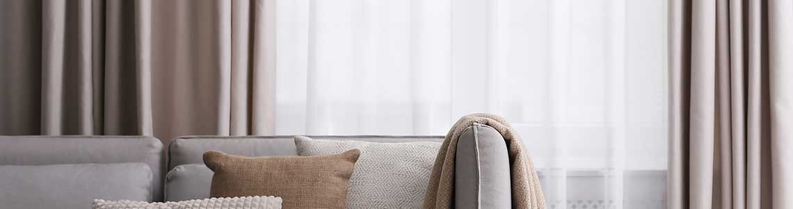 Massvorhänge (Vorhänge nach Mass) mit Sofa mit Kissen und Plaids.